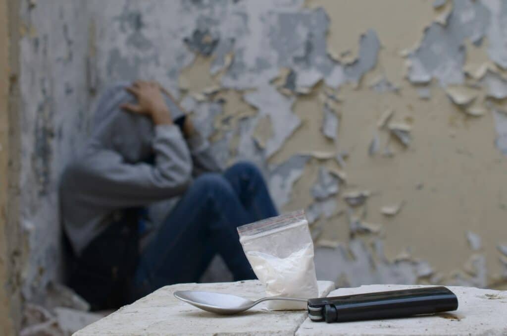 A drug-dependent man suffers from drug withdrawal while sitting in abandoned building next to dose