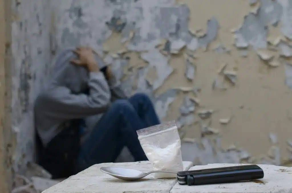 A drug-dependent man suffers from drug withdrawal while sitting in abandoned building next to dose