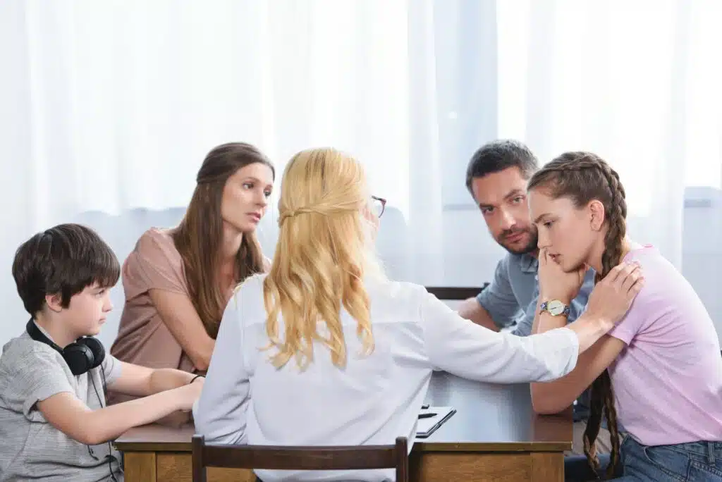 rear view of female counselor cheering up upset teenage girl on family therapy session in office